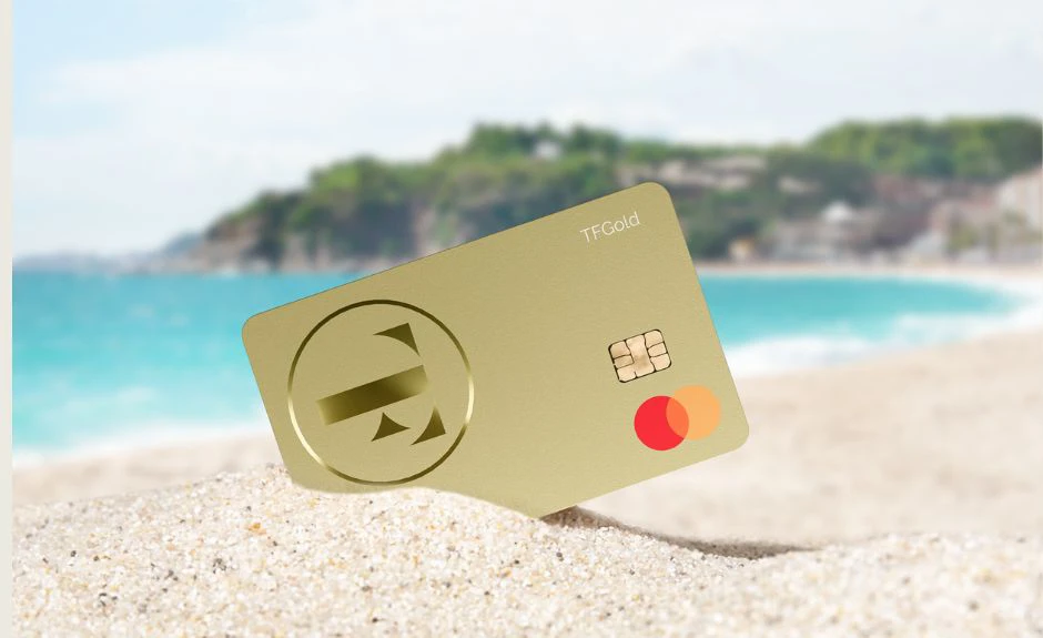 Carta di credito TF Mastercard Gold sulla sabbia, con vista del mare sullo sfondo