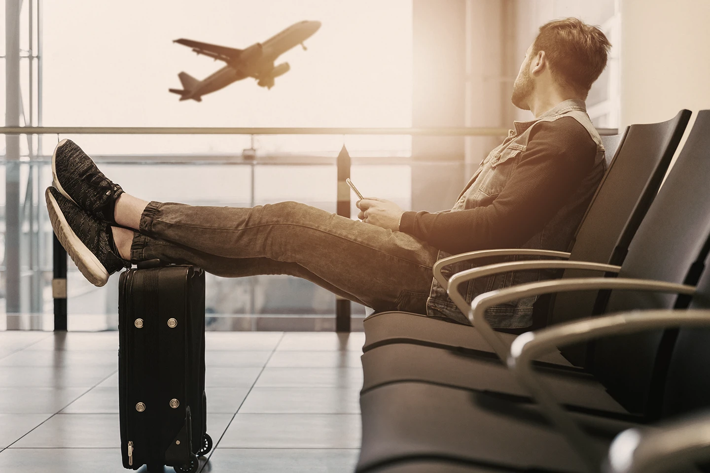 Hombre esperando su vuelo en el aeropuerto. Al fondo, se ven aviones despegando.