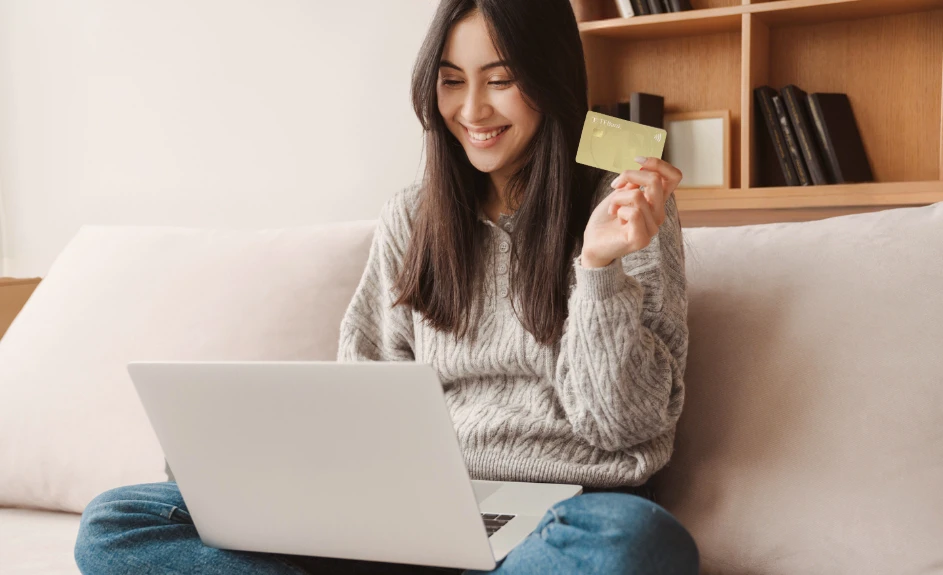 ragazza che tiene in mano la sua carta di credito seduta davanti al computer