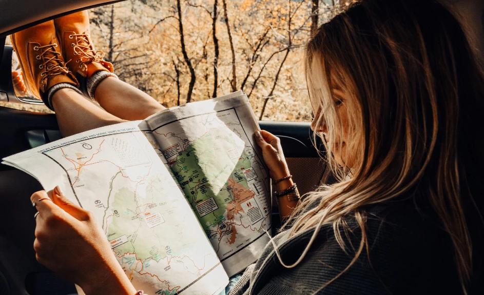 Ragazza in macchina controllando il percorso su una mappa stampata