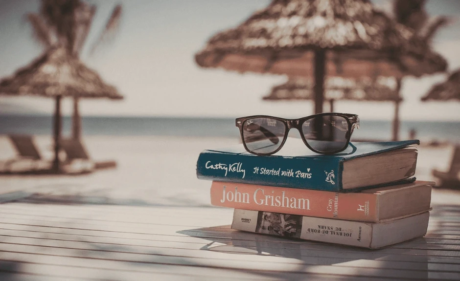 Foto de vacaciones mostrando gafas de sol y un libro con el océano de fondo.