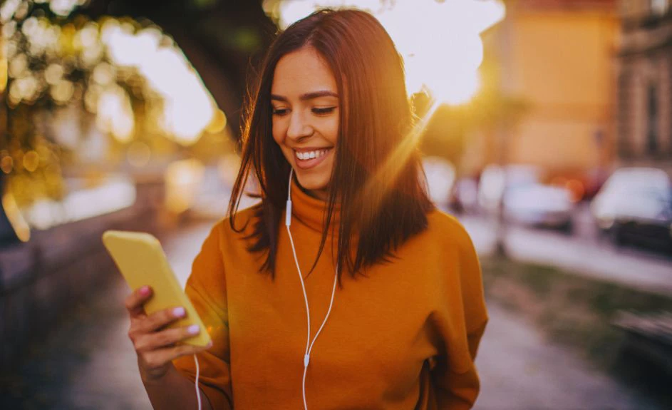 ragazza che guarda il telefono e ascolta musica, sullo sfondo si vede il tramonto
